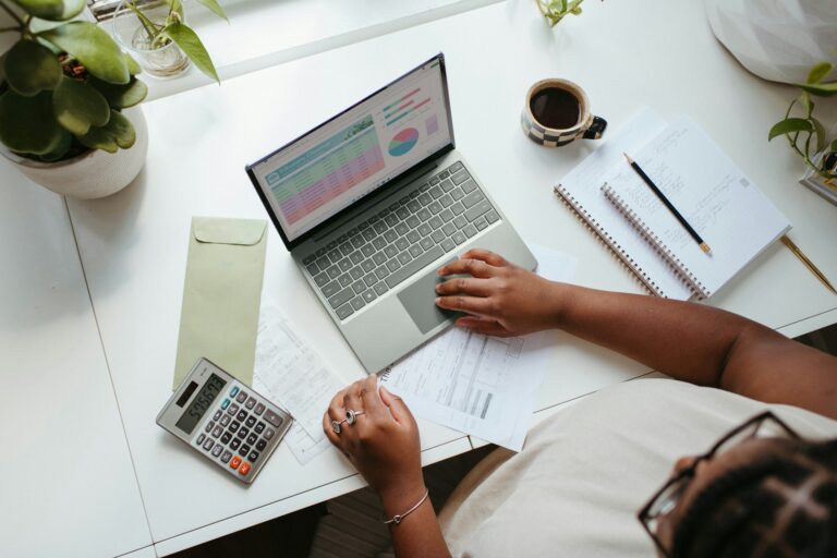 Business owner reviewing costs on a laptop with a calculator and paperwork